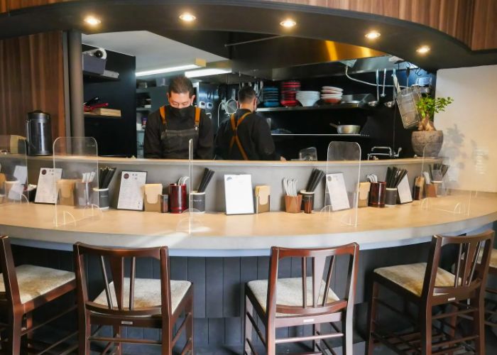 The counter seating at Ramen Break Beats, where two chefs can be seen cooking in the kitchen.